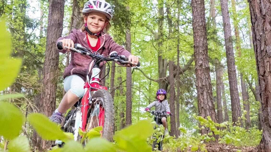 Zwei Kinder fahren mit Fahrrädern durch einen Wald. Sie tragen Helme und lachen, während sie die Natur genießen. | © 3Eiben Kids Bike Park