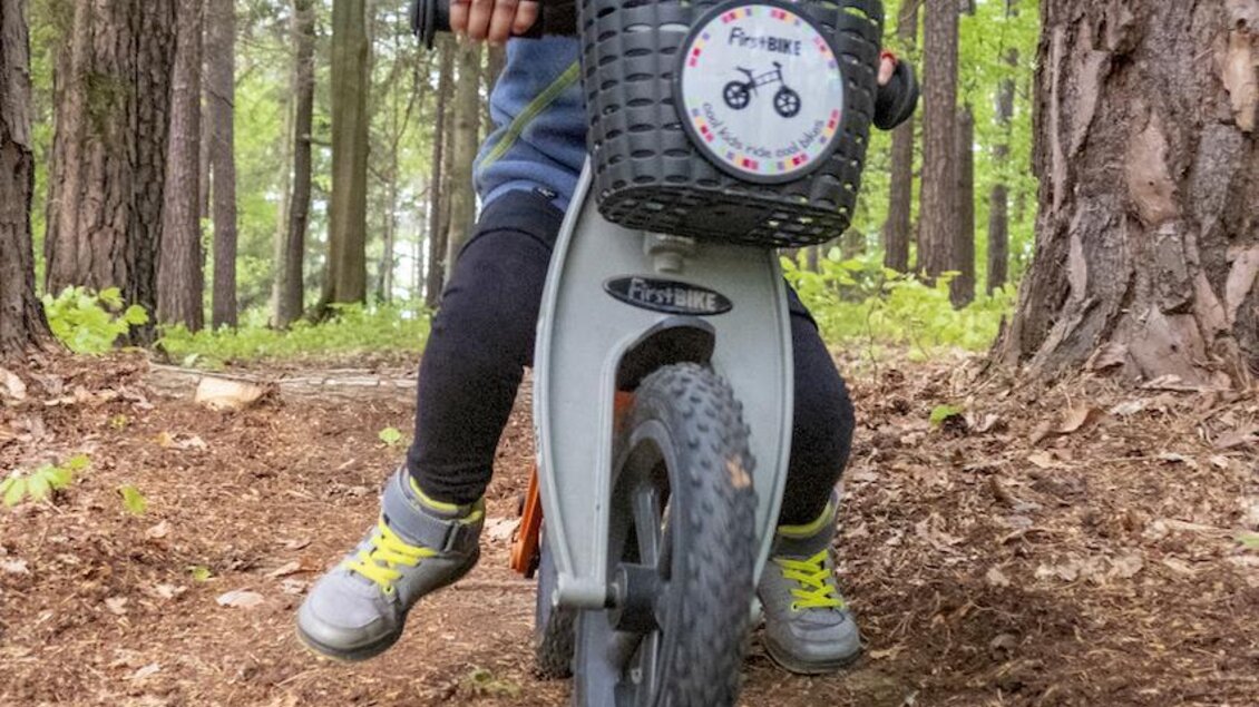 Ein lachendes Kind fährt auf einem Balancebike durch den Wald. Umgeben von grünen Bäumen und Erde hat es einen Fahrradhelm auf. | © 3Eiben Kids Bike Park
