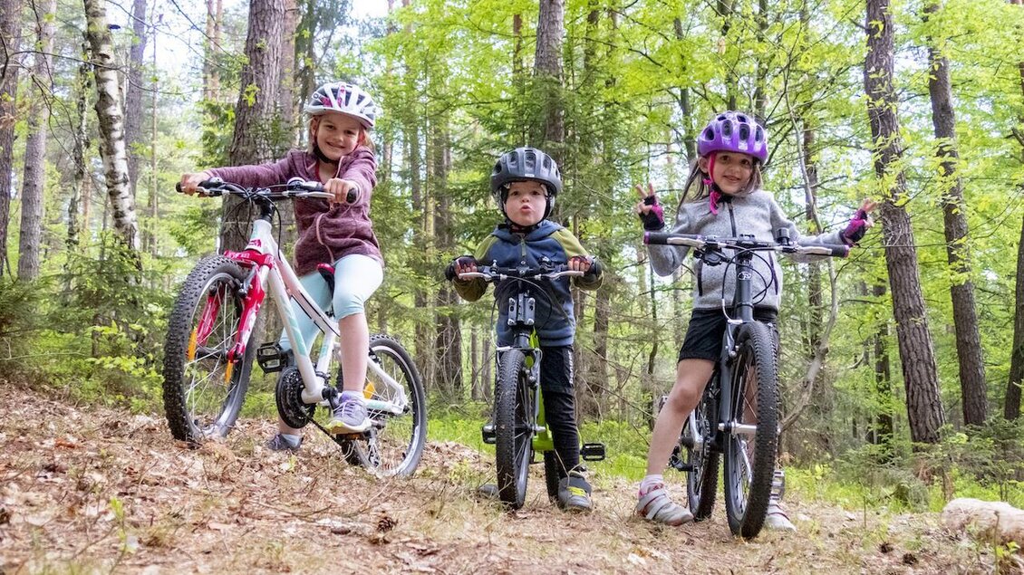 Drei Kinder stehen mit ihren Fahrrädern im Wald. Sie tragen Helme und freuen sich über ihre Fahrradausflüge. | © 3Eiben Kids Bike Park