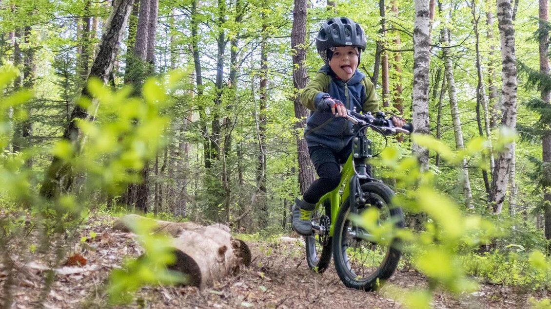 Ein Junge fährt mit einem Fahrrad durch den Wald. Er trägt einen Helm und hat Freude am Radfahren. | © 3Eiben Kids Bike Park