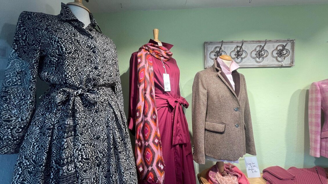 Elegante Mode in einem Geschäft. Verschiedene Kleidungsstücke, einschließlich eines gemusterten Kleides, einer Schal und eines Blazers, sind ausgestaltet. | © TVB Ausseerland-Salzkammergut_Nathalie Schröttenhamer