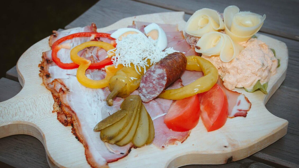 Eine leckere Zusammenstellung von Wurst, Käse und Gemüse auf einem Holzbrett. Die frischen Zutaten sind farbenfroh angeordnet und laden zum Essen ein. | © Lederer