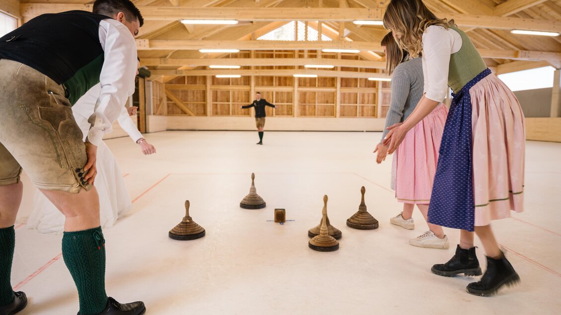 Eine Gruppe von Menschen spielt eine Spiel mit Holzklötzen auf einer glatten Fläche. Im Hintergrund ist ein weiteres Mitglied der Gruppe, das den Wurf vorbereitet. | © www.zloam.at