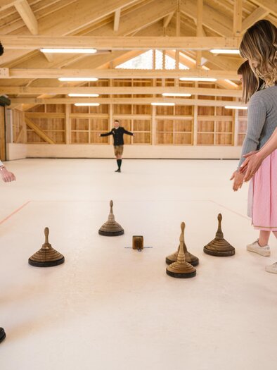 A group of people is playing a game with wooden blocks on a smooth surface. In the background, there is another member of the group preparing to throw. | © www.zloam.at