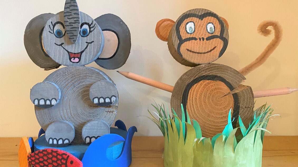 Eine kreative Bastelarbeit mit einem Elefanten und einem Affen aus Pappe. Der Elefant sitzt in einem blauen Wasserbereich, während der Affe in einem grünen Grasring steht. | © www.zloam.at