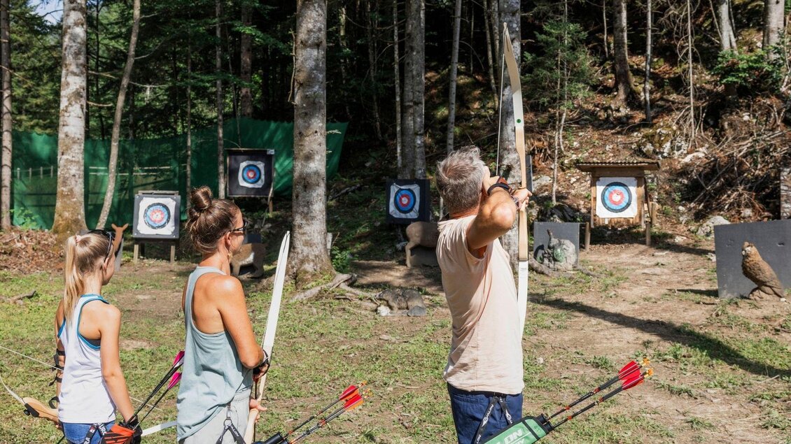 Eine Gruppe von Personen übt das Bogenschießen im Freien. Sie stehen vor Zielscheiben, umgeben von Bäumen und Natur. | © www.zloam.at