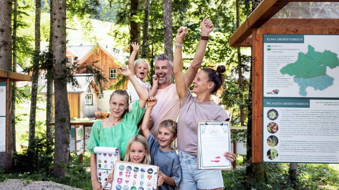 Eine fröhliche Familie steht in der Natur und feiert ihren Erfolg. Sie halten Urkunden und Aufkleber in den Händen und lächeln in die Kamera. | © www.zloam.at