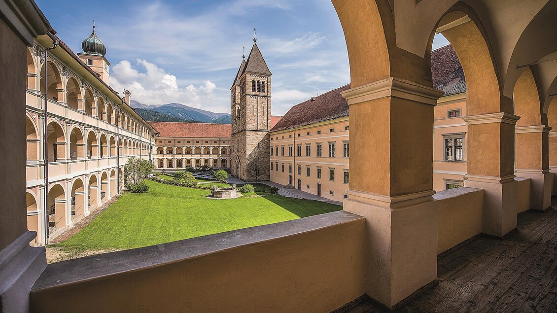 Ein wunderschöner Innenhof eines Klosters mit einem grünen Rasen und einem beeindruckenden Turm. Die Architektur umrahmt den Hof mit Bögen und Säulen. | © Abtei Seckau