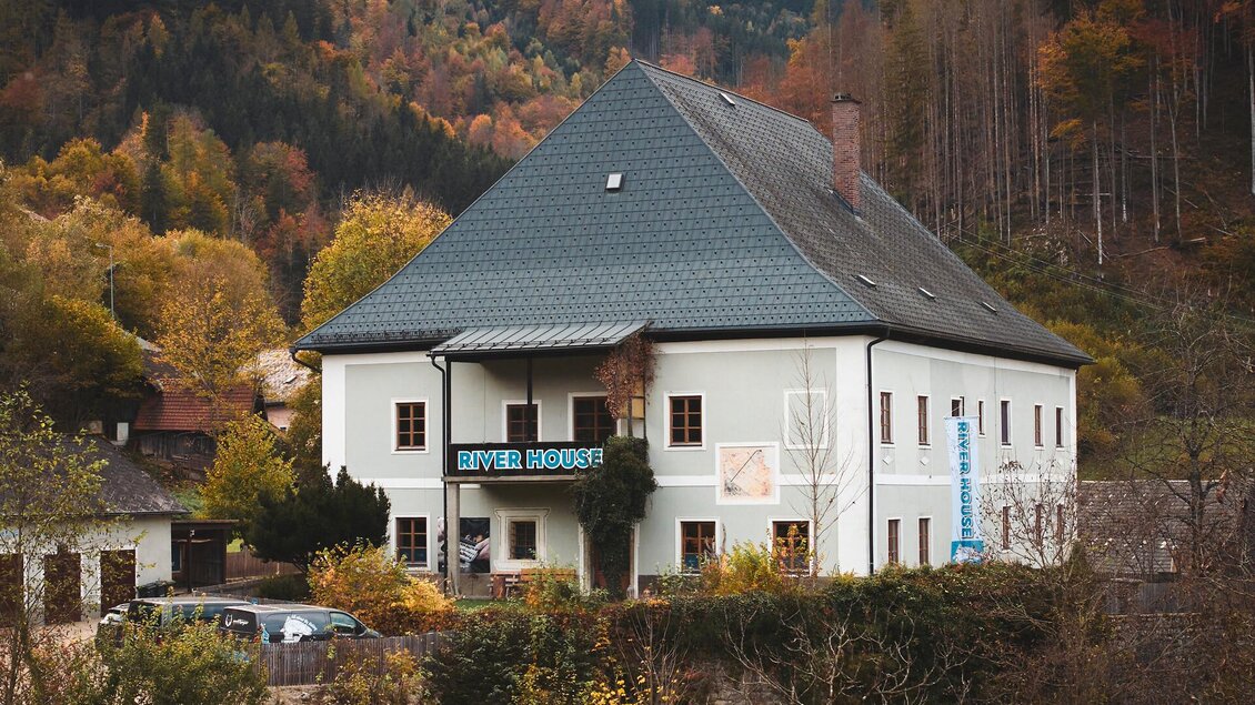Ein charmantes Gebäude umgeben von buntem Herbstlaub. Das Haus hat einen traditionellen Stil und steht in einer waldreichen Umgebung.