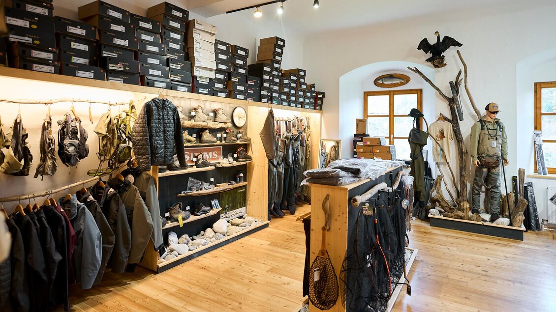 Ein Laden mit Jagdbekleidung und Ausrüstung. An den Wänden hängen Kleidungsstücke, während Regale mit Schuhen und Zubehör gefüllt sind.