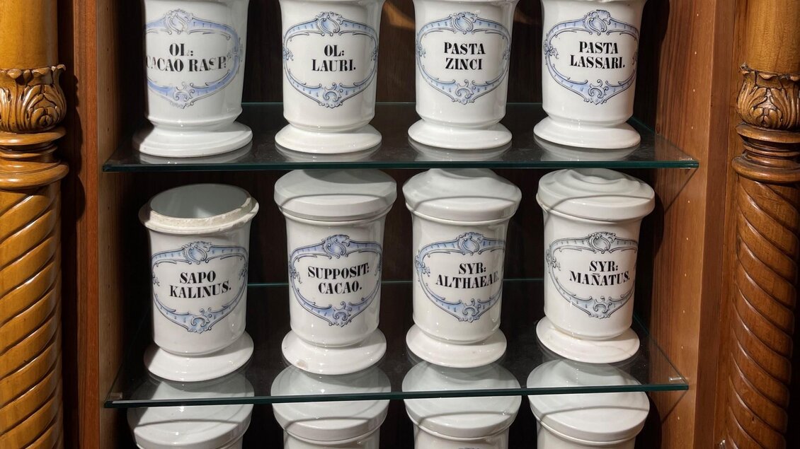 Weiße Porzellangefäße mit lateinischen Aufschriften in Holzvitrine im Adler Apotheken Museum Graz | © Adler Apotheken Museum