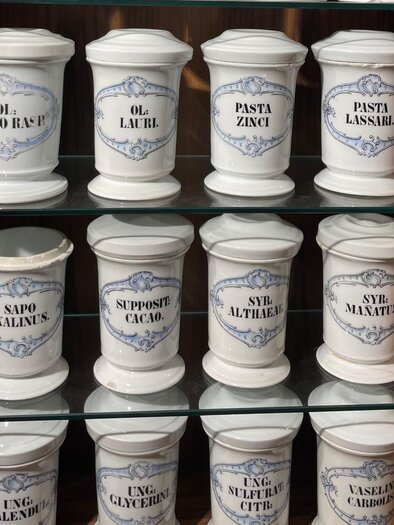 Weiße Porzellangefäße mit lateinischen Aufschriften in Holzvitrine im Adler Apotheken Museum Graz | © Adler Apotheken Museum