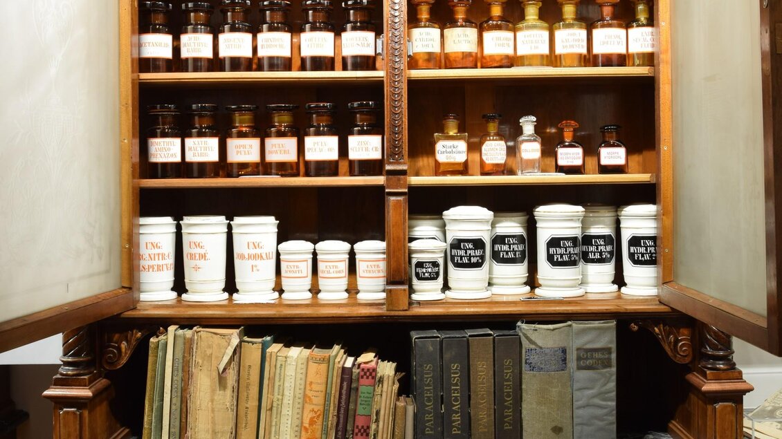 Historischer Apothekenschrank mit Arzneigläsern, Porzellangefäßen und alten Büchern im Adler Apotheken Museum Graz | © Adler Apotheken Museum