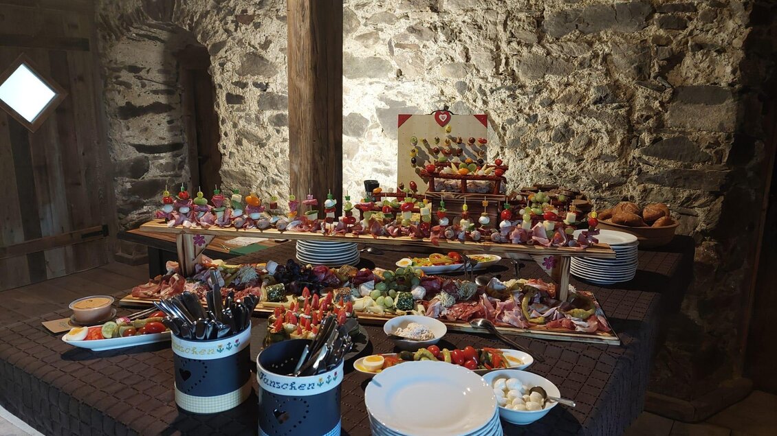 Ein reichhaltiges Buffet mit verschiedenen Häppchen und appetitlichen Speisen. Im Hintergrund sind Steinwände sichtbar, die eine rustikale Atmosphäre schaffen. | © Erwin Troger