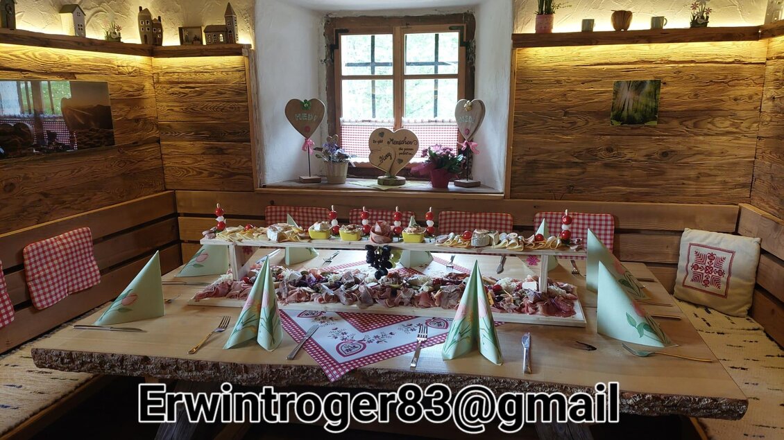 Ein rustikaler Essraum mit einem großen Tisch, der reichlich mit verschiedenen Speisen und Dekorationen gedeckt ist. Die warmen Holzwände und das Licht schaffen eine gemütliche Atmosphäre. | © Erwin Troger