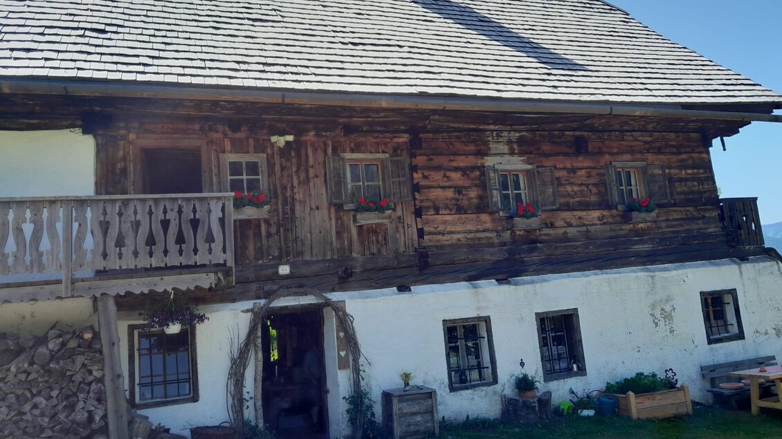 Ein traditionelles altes Holzhaus mit einem dekorativen Balkon und Blumen in den Fenstern. Es hat eine rustikale Fassade und befindet sich in einer ländlichen Umgebung. | © Erwin Troger