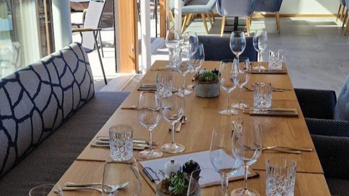 Ein eleganter Restauranttisch mit Tischgedeck, Gläsern und Besteck ist vorbereitet. Im Hintergrund sind gemütliche Sitzgelegenheiten und große Fenster, die viel Licht hineinlassen. | © Sophie Dekkers