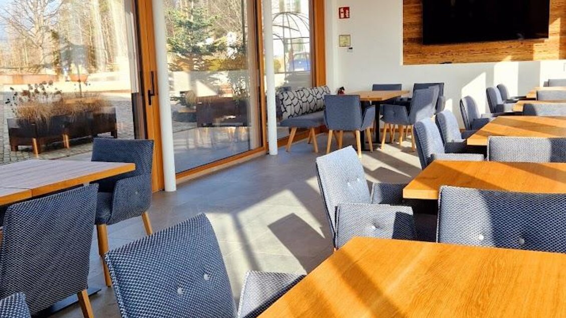 Ein modernes Restaurant mit Holzboden und großen Fenstern. Die Einrichtung ist schlicht und einladend, mit Holz- und blauen Stühlen. | © Almerwirt