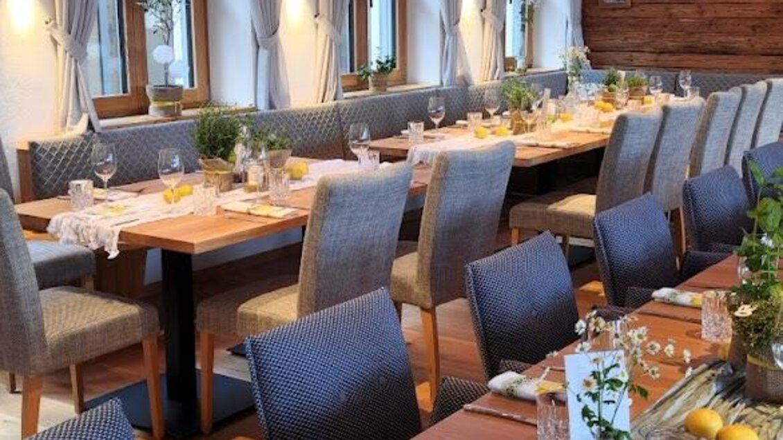 Ein gemütlicher Speisesaal mit langen Holztischen und blauen Stühlen. Die Atmosphäre ist einladend mit dekorativen Elementen und sanfter Beleuchtung. | © Almerwirt