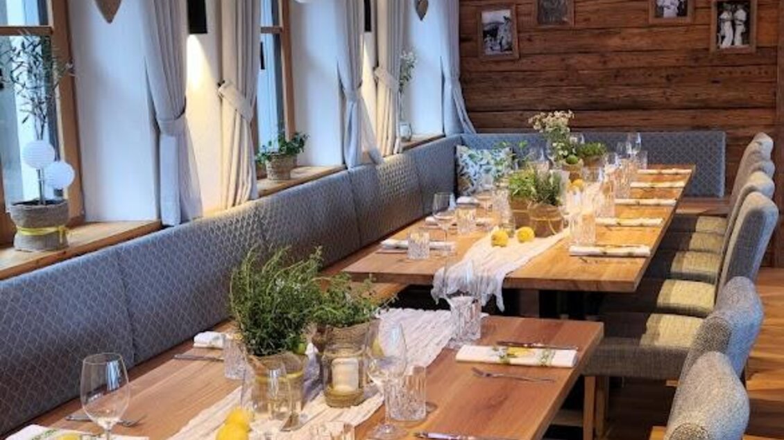 Ein gemütliches Restaurant mit langen Tischen und modernen Stühlen. Die Tische sind festlich gedeckt und die Wände sind aus Holz. | © Almerwirt