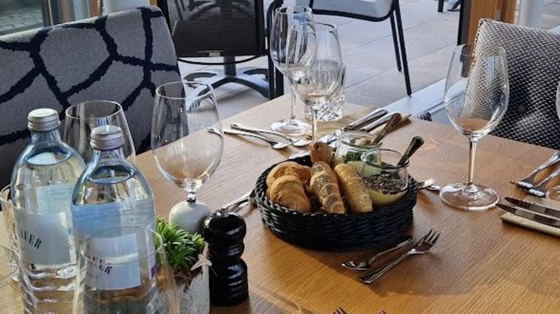 Ein elegantes Restaurant mit einem schön gedeckten Tisch. Auf dem Tisch stehen Wasserflaschen, Gläser und eine kleine Auswahl an Speisen. | © Almerwirt