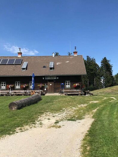Ein gemütliches Bauernhaus mit einem großen Garten und Rundweg. Im Hintergrund sind Bäume und ein blauer Himmel zu sehen. | © K. Fleck