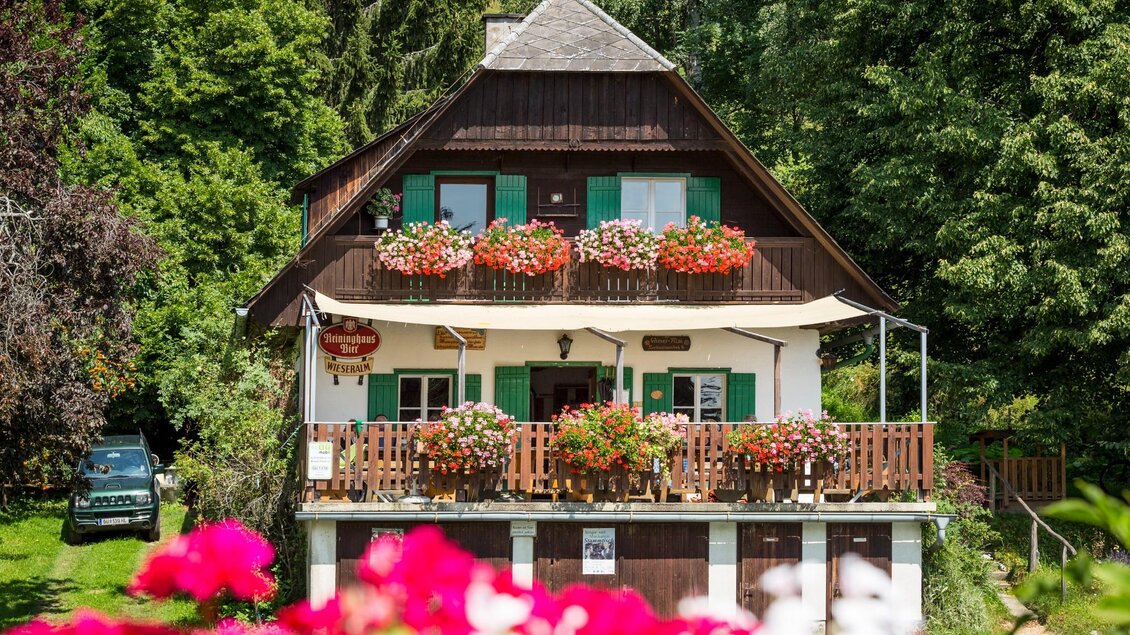 Holzhaus mit Blumenschmuck und Sonnenterrasse umgeben von grünen Wäldern | © TV Region Graz - René Vidalli
