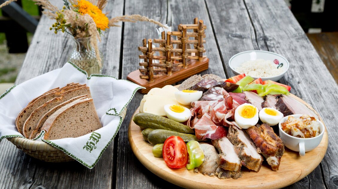Ein rustikales Tischarrangement mit einer Auswahl an Aufschnitt, eingelegtem Gemüse und Eiern. Neben dem Essen befinden sich frisches Brot und eine dekorative Platzierung auf dem Tisch. | © TV Region Graz - René Vidalli
