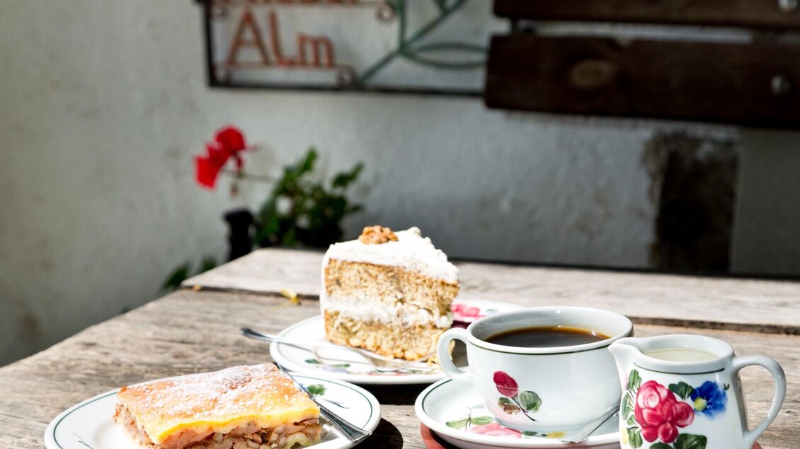 Zwei Stück Kuchen und eine Tasse Kaffee auf Holztisch im Freien bei Sonnenschein | © TV Region Graz - René Vidalli