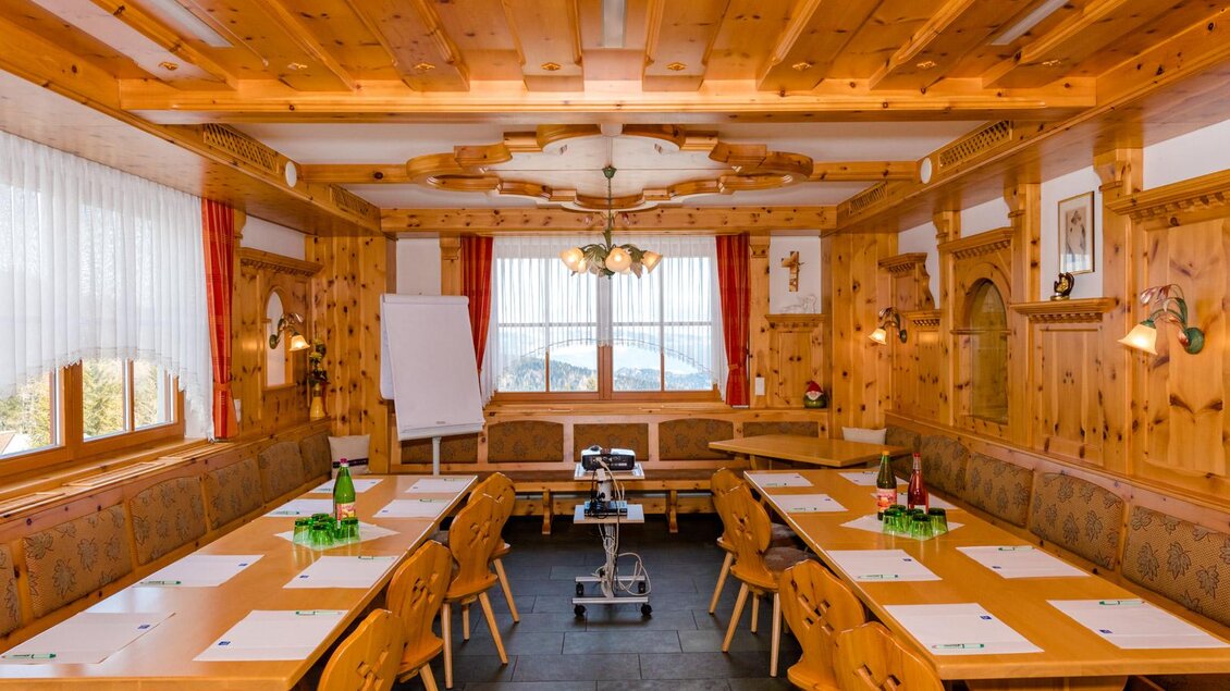 Ein gemütlicher Seminarraum mit Holzwänden und rustikalen Möbeln. Auf den Tischen sind Wasserflaschen und Notizblätter vorbereitet. | © Almidylle Sabathy