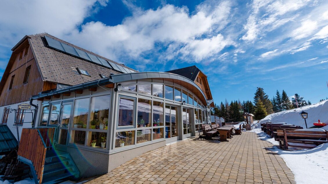 Ein modernes Gebäude am Hang, umgeben von Schnee und Bäumen. Der Himmel ist blau mit einigen Wolken. | © Almidylle Sabathy