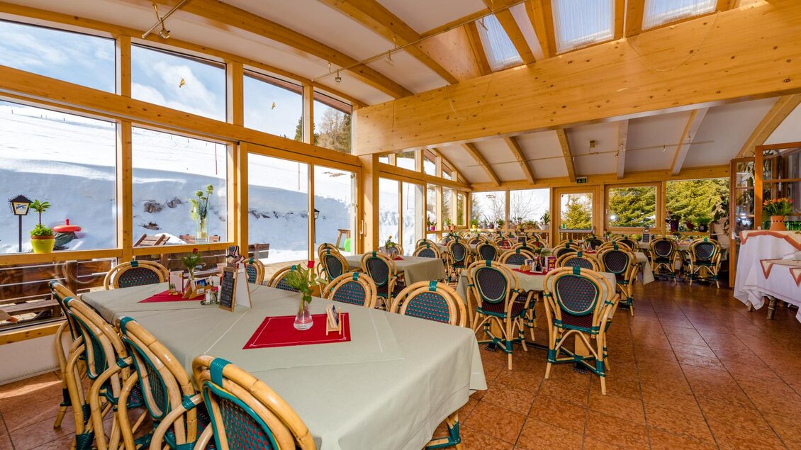 Ein einladendes Restaurant mit großen Fenstern und Blick auf die Natur. Die Tische sind festlich gedeckt und die Einrichtung ist gemütlich. | © Almidylle Sabathy