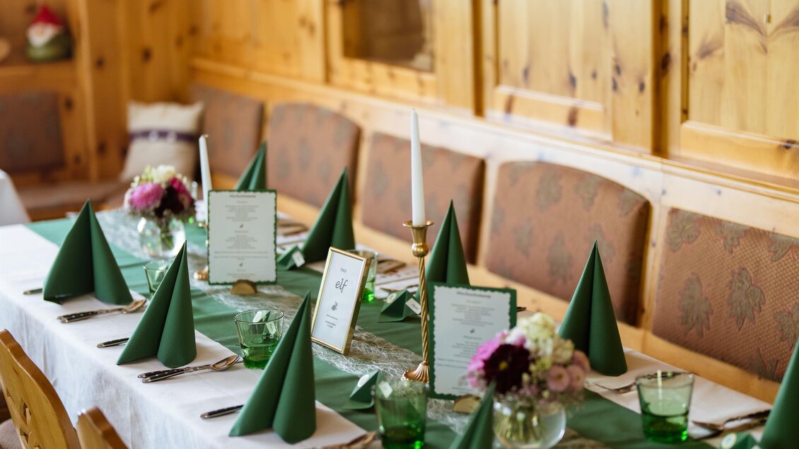 Ein festlich gedeckter Tisch in einem Holzraum mit grünen Servietten und Blumen. Die Atmosphäre ist gemütlich und einladend. | © Almidylle Sabathy