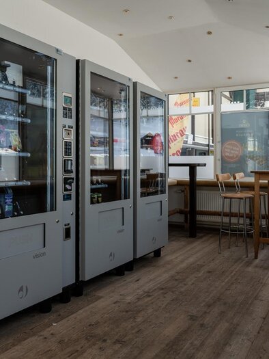 A modern lounge area with two vending machines and a wooden table. Large windows provide plenty of daylight. | © TMG Turracher Höhe Marketing GmbH