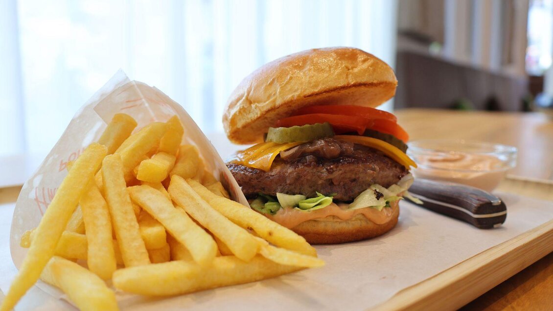 Ein leckerer Hamburger mit frischem Gemüse und Käse, serviert mit knusprigen Pommes frites. Das Gericht liegt auf einem hellen Tablett in einem gemütlichen Umfeld. | © Gerhard Wolkersdorfer