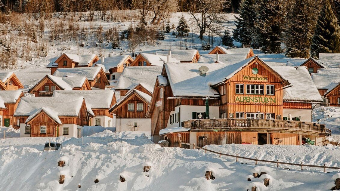 Eine malerische Winterlandschaft mit schneebedeckten Hütten. Im Vordergrund steht ein charmantes Holzgebäude mit dem Namen „Alpenstüble“. | © Alpenstubn