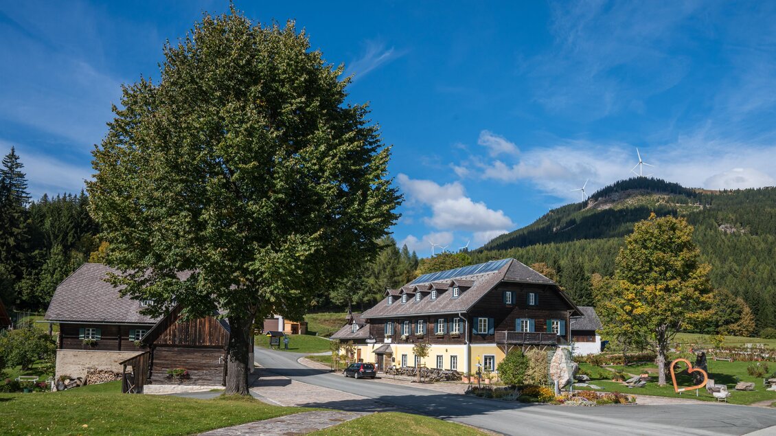 Eine malerische Landschaft mit einem historischen Gebäude und großen Bäumen. Im Hintergrund sind sanfte Hügel und ein blauer Himmel zu sehen. | ©  Christian Freyd