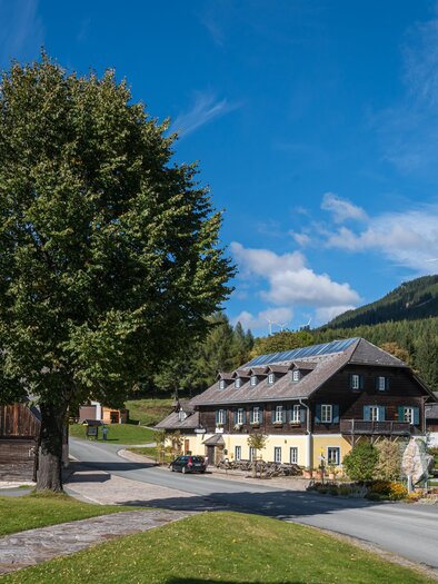 A picturesque landscape with a historic building and large trees. In the background, gentle hills and a blue sky can be seen. | ©  Christian Freyd
