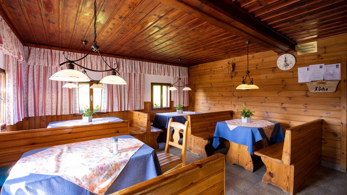 Ein gemütlicher Innenraum mit Holzmöbeln und blauen Tischdecken. Die Wände sind mit Holz verkleidet, und es gibt sanfte Beleuchtung sowie Fenster mit Vorhängen. | © TV Region Graz-Harry Schiffer