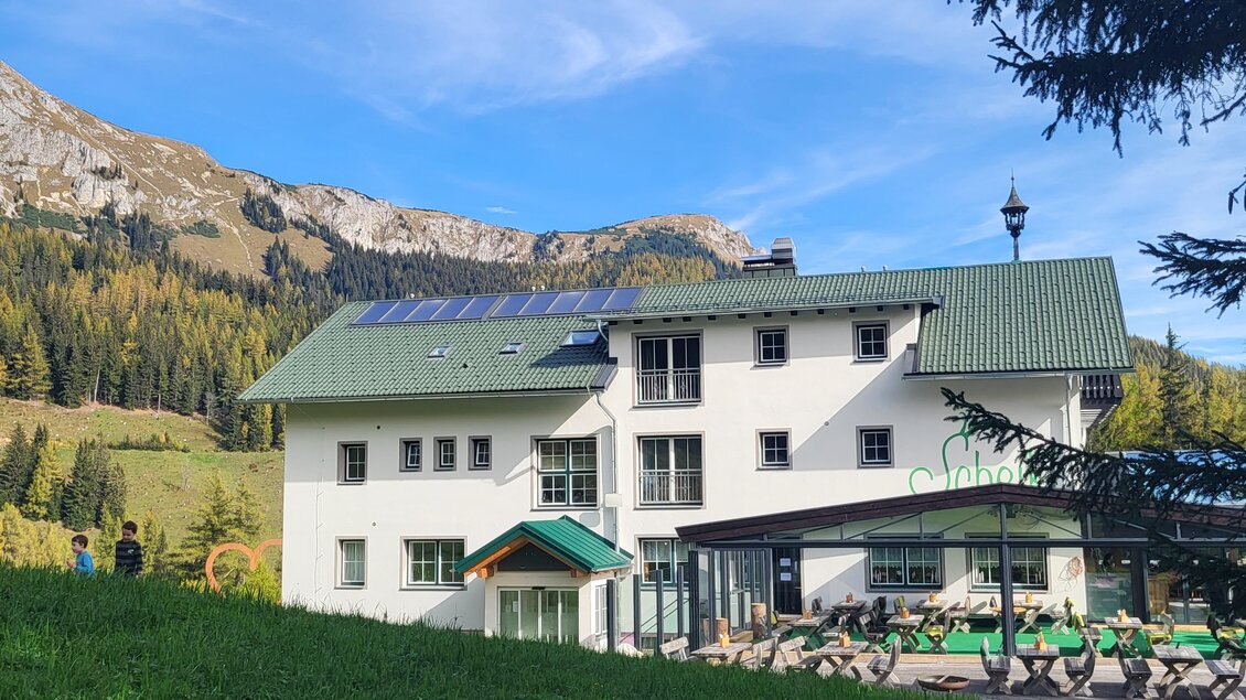 Ein modernes Gebäude in den Bergen, umgeben von Wiesen und Bäumen. Im Hintergrund sind beeindruckende Berge zu sehen. | © TV Hochsteiermark