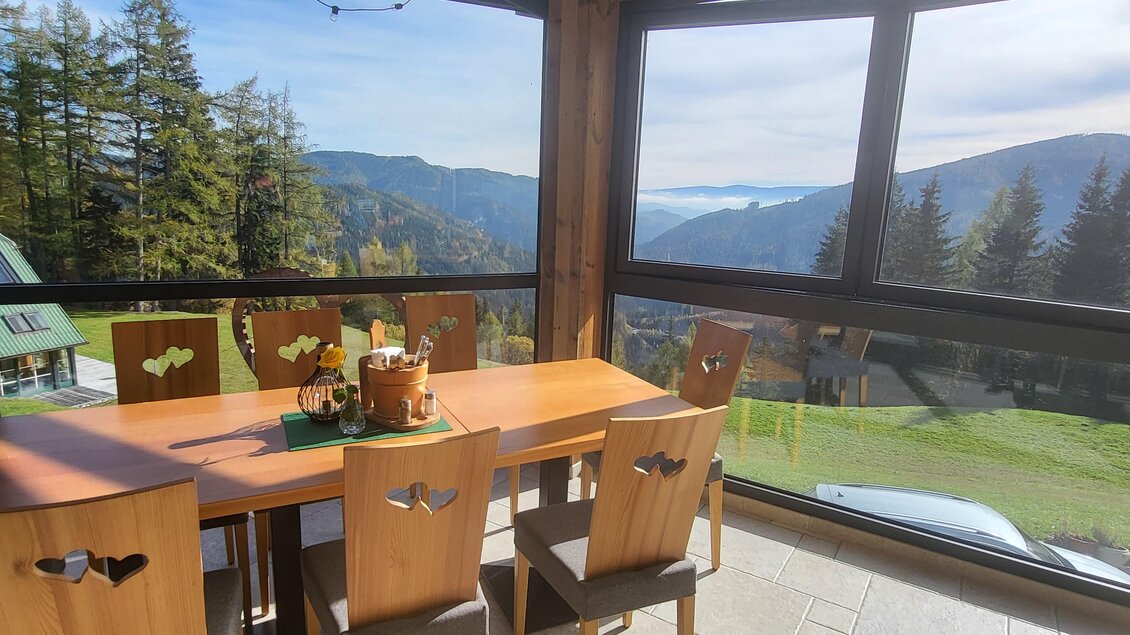 Ein schöner Essbereich mit Holzstühlen und Tisch, umgeben von großen Fenstern. Der Blick auf die Berge und die Natur bietet eine entspannende Atmosphäre. | © TV Hochsteiermark