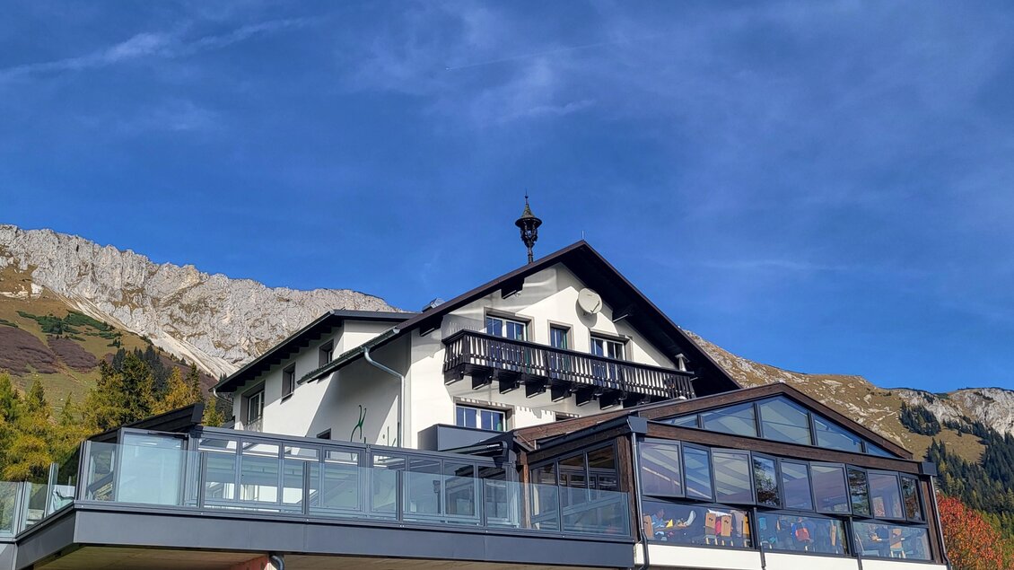 Ein modernes Haus mit großen Fenstern und einem Balkon in den Bergen. Im Hintergrund sind hohe Bergrücken und ein klarer Himmel zu sehen. | © TV Hochsteiermark