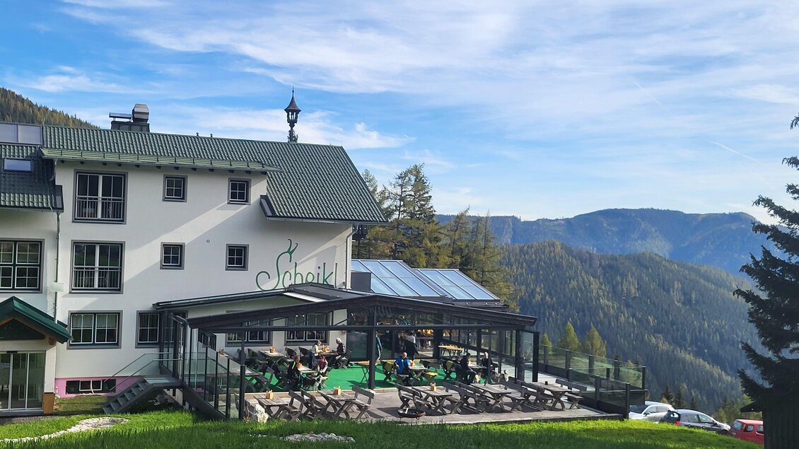 Ein malerisches Restaurant in den Bergen mit einer Terrasse. Im Hintergrund sind grüne Wiesen und bewaldete Hügel zu sehen. | © TV Hochsteiermark