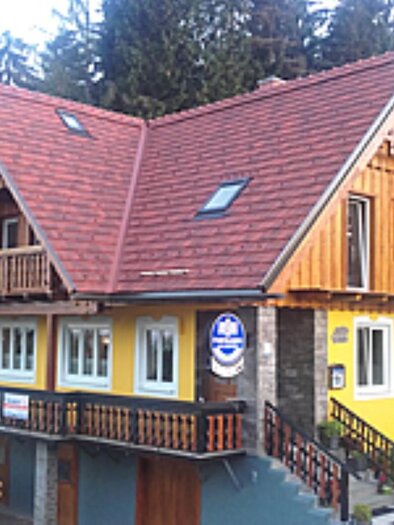 A cozy house with a red roof and yellow facade. Surrounded by trees, it conveys an inviting atmosphere. | © Alpengasthof Strutz