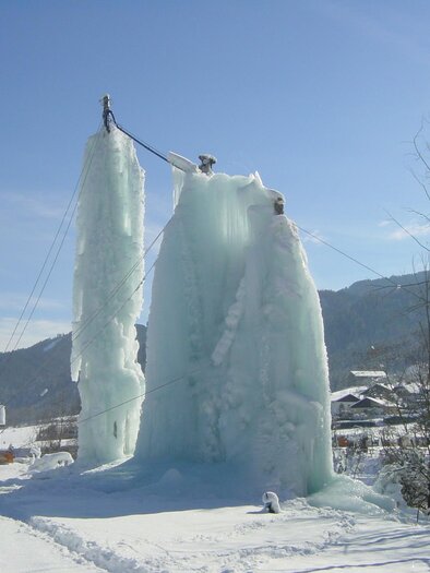 An impressive ice formation next to a building in winter. The ice sculptures tower high into the blue sky. | © Erlebnisregion Murtal