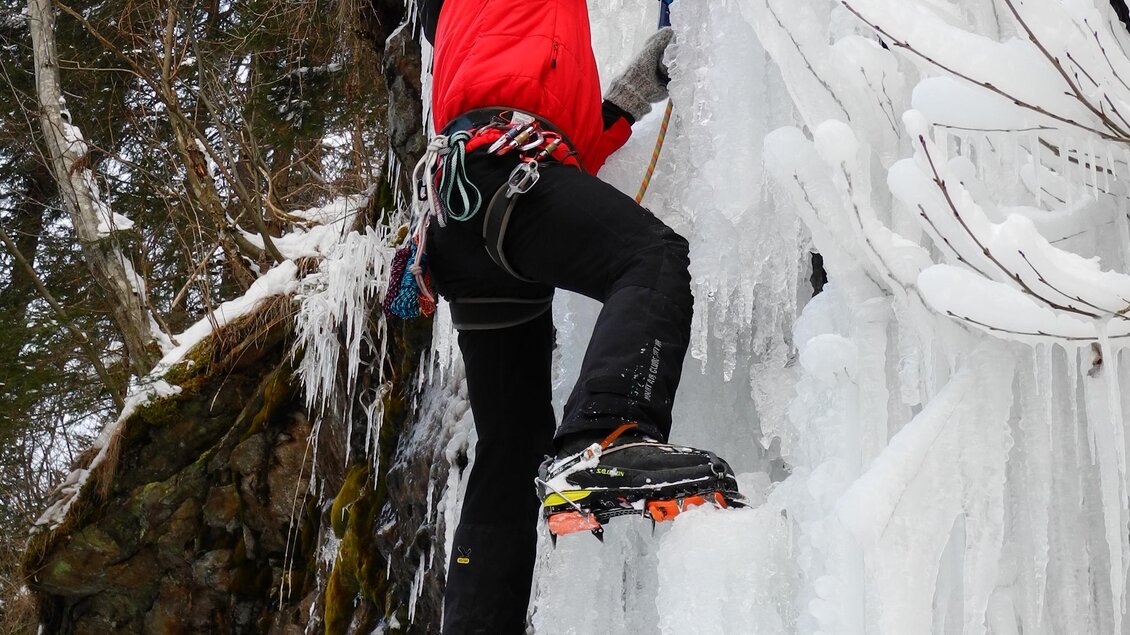 Ein Kletterer in roter Jacke erklimmt eine gefrorene Wasserfallwand. Die Eisformationen sind beeindruckend und umgeben von schneebedeckten Felsen und Bäumen. | © Erlebnisregion Murtal
