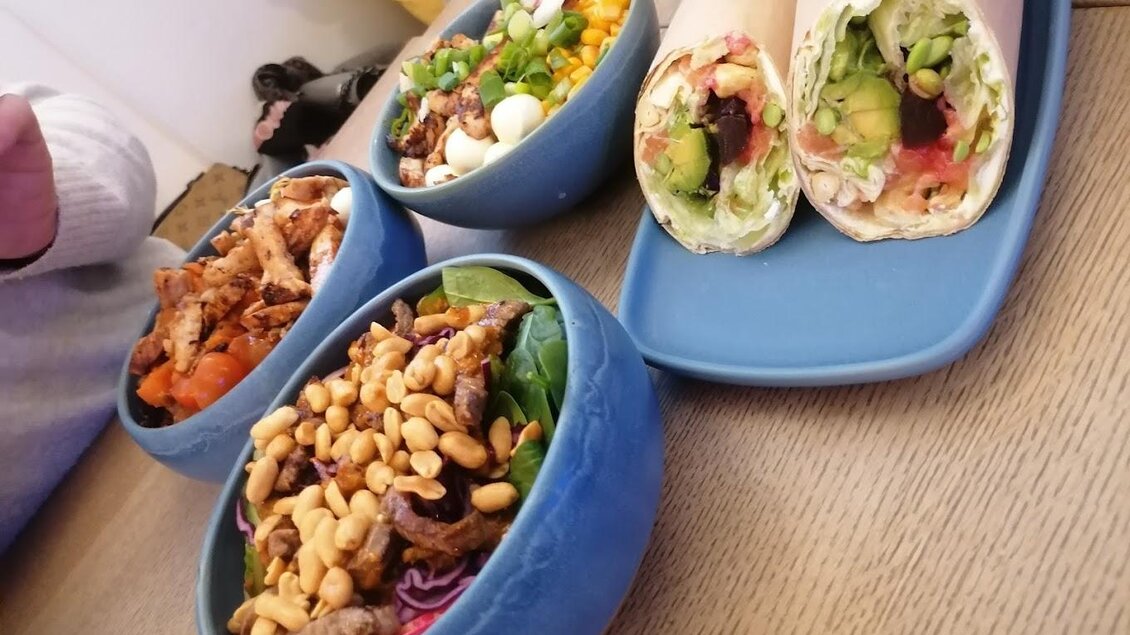 Ein Tisch mit verschiedenen Schalen voller bunter Salate und zwei Wraps. Frische Zutaten und eine ansprechende Präsentation machen das Essen appetitlich. | © Alpoke - K.van Kerken