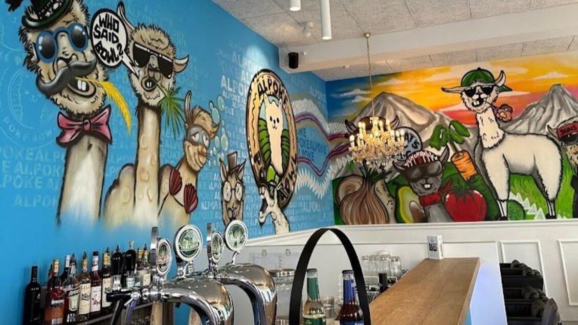 Eine kreative Bar mit einer farbenfrohen Wandmalerei von Lamas. Der Tisch und die Bar sind modern gestaltet, ideal für gesellige Treffen. | © Alpoke - K.van Kerken