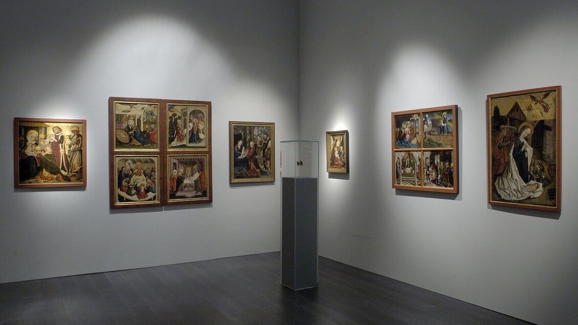 Ein Ausstellungsraum in der Alten Galerie mit mehreren Gemälden an den Wänden. In der Mitte steht ein Glasdisplay mit weiteren Kunstwerken. | © UMJ