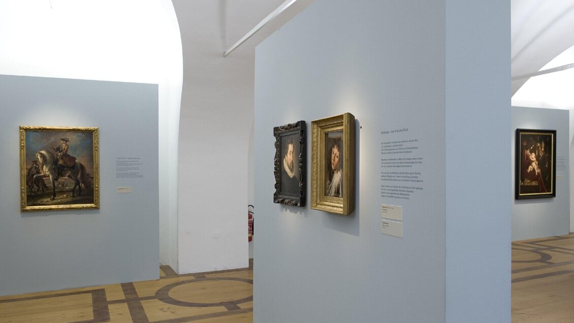 Die Alte Galerie mit mehreren Bildern an hellblauen Wänden. Der Boden ist aus Holz und die Beleuchtung ist sanft. | © UMJ